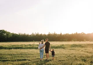 A happy woman and man walking hand in hand with their child, through a green field on a sunny day.