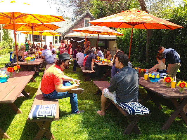 Guests at an outdoor baby shower orange umbrellas benches COCOCOZY logo throw