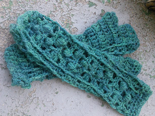 Two crochet fingerless mittens laying on top of each other.  They are worked in fingering-weight yarn.   The mitten on top has a lace and bobbles stitch on the back of the hand, mitten below is palm up, with alternating rows of single crochet and double crochet.  There is a grey cat paw in the top right corner. 