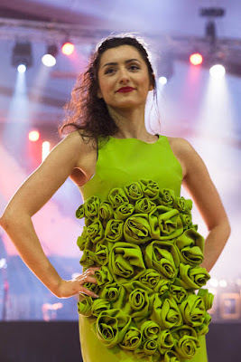 Jeune femme mannequin à un défilé, vêtue d'une robe vert-jaune agrémentée sur le devant de fleurs en tissu de même couleur.