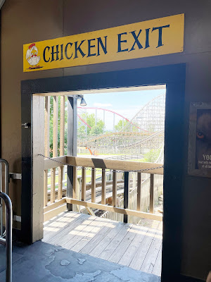 An open doorway with a rollercoaster in the background. Above the doorway is a yellow sign that reads, "Chicken Exit."