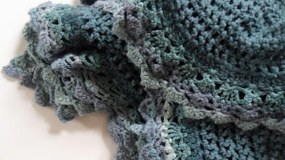 Crochet shawl, chunky wool with contrasting lace edge. Colours go from dark aqua to light aqua through different shades of blue