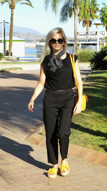 Alejandra Colomera con camiseta negra, pantalón formal negro, lazo en el cuello negro con lunares blancos y complementos mostaza