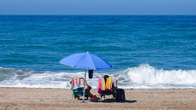 Una sombrilla y dos sillas mirando al mar de aguas azules con oleaje un día soleado de verano