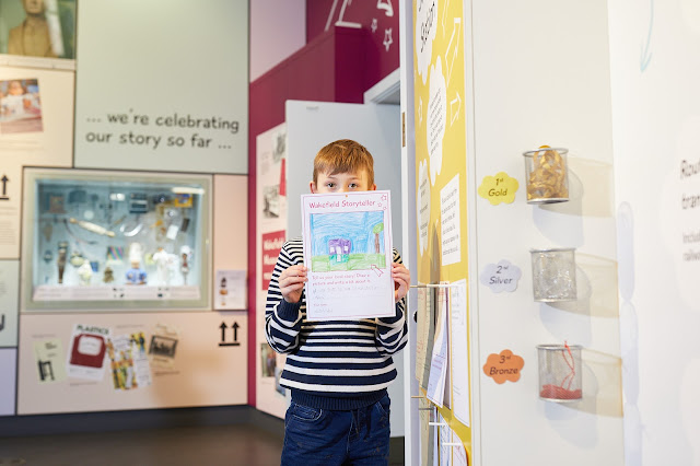 A young visitor holding their drawing up to the camera in Moving Stories at Wakefield Museum