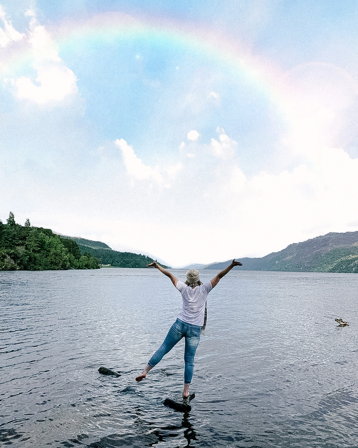 Travel blogger standing on the edge of Loch Ness in Scotland losing at a rainbow