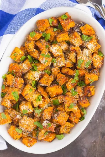 Top view of parmesan herb roasted sweet potatoes in a white oval dish.