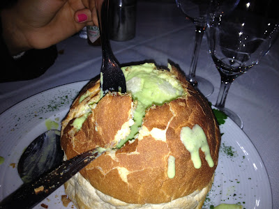 A foto mostra um pão bem grande, com um furo no meio, completo com creme de ervilha. A Stephanie está cravando o garfo no pão para começar a comer. Foto tirada no restaurante Petit Brasil, em Gramado RS.