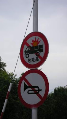 Image of two more road signs, on the same pole, in China. One sign is of an exploding truck.