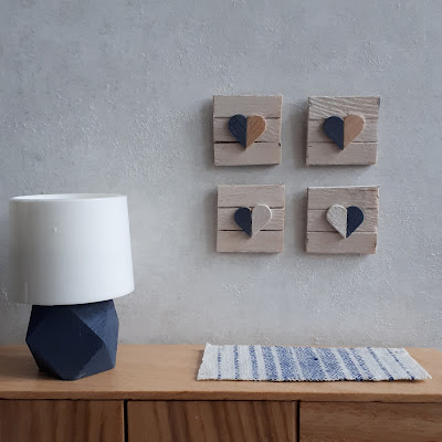One-twelth scale modern miniature  sideboard with a lamp on it and framed wooden heart shapes on the wall above it.