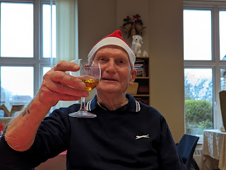 My dad wearing his santa hat and holding up a glass of apple juice to says cheers to everyone at the table who are out of shot for privacy reasons