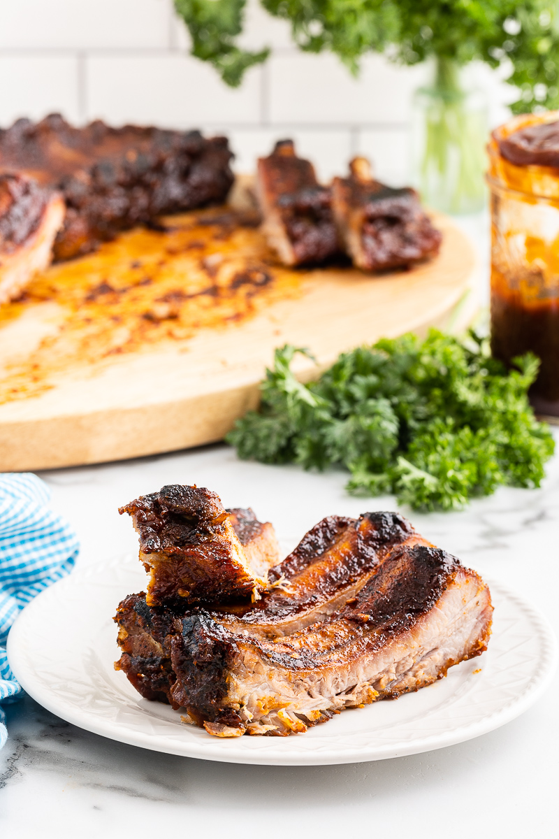 Keto BBQ ribs on a white plate with more rib on a wooden cutting board in the background.