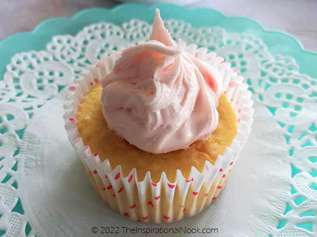 Cupcake with pink frosting on a paper doily on a turquoise plate