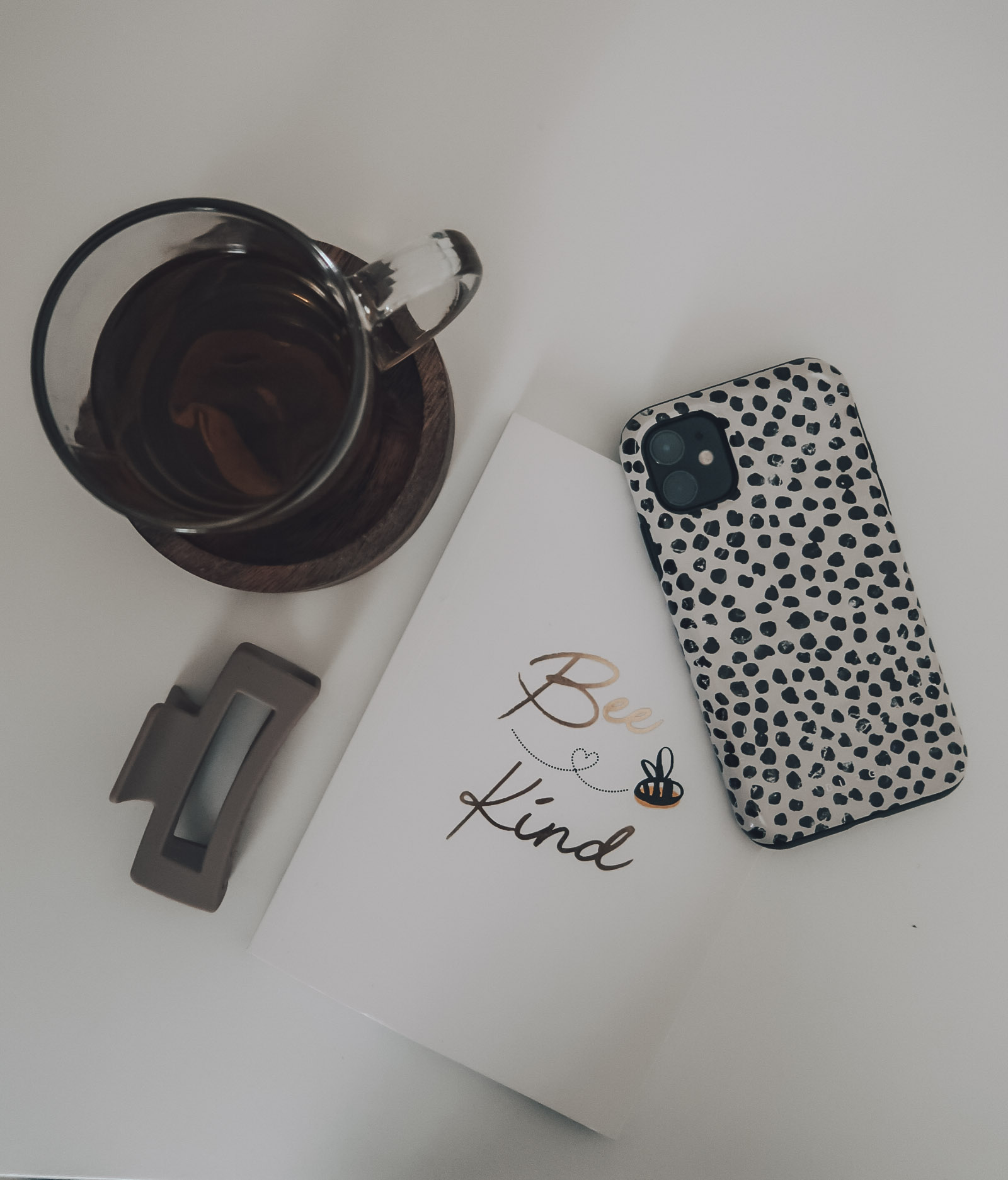 A 'Bee Kind' notebook, Iphone, mug of tea and beige hairclip.