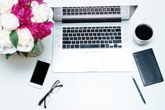 Computer, coffee mug, wallet, black pen, eye glasses, mobile phone and a vase of flowers arranged on top of a white work table.