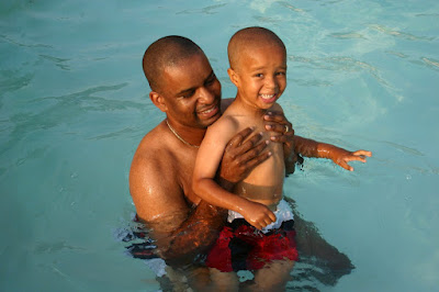 Image of a happy man in the water holding a happy child. Here are some tips to help your child learn to swim sooner.