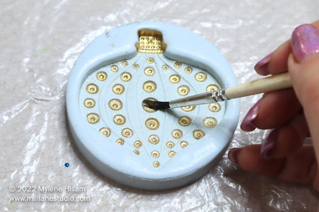 Hand holding paintbrush, brushing gold powder onto the detail of a silicone bauble mould