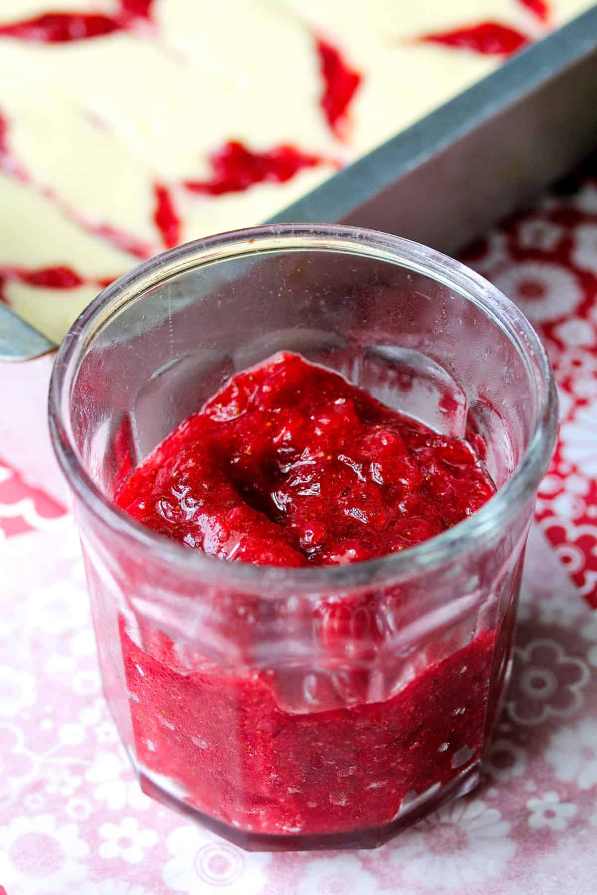 Strawberry jam in a jelly jar with cheesecake in the background.