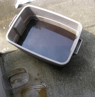 Large plastic container with leftover coffee grounds and water added.