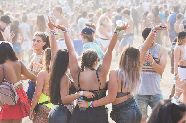 Three girls gets picture taken in music festival with people