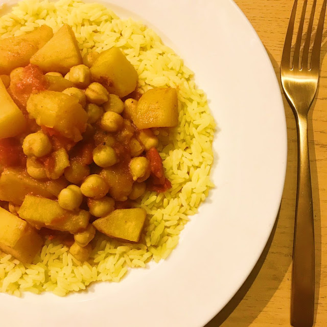 slow cooker potato and chickpea curry on top of turmeric rice. Gold cutlery next to plate