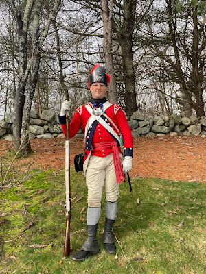 A reenactor in a scarlet coat, white breeches and leather helmet depicts a light infantry officer of the British 4th Regiment of Foot.