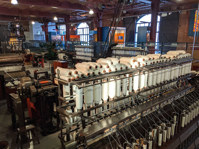 Cotton bobbins on a metal frame with textiles machinery in background