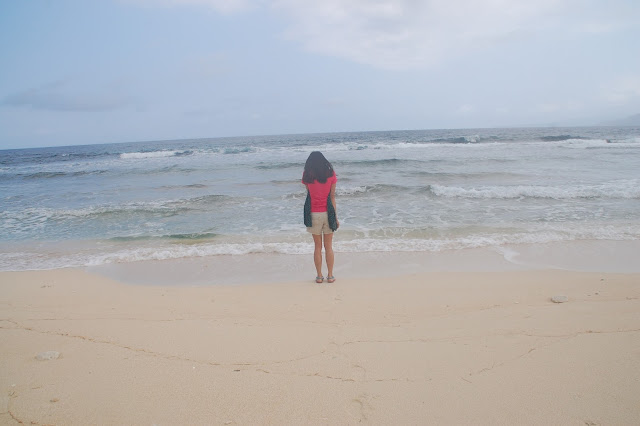 Girl stands with her back towards the camera at Nakabuang Beach while the wind blows through her hair and waves crash to the beach