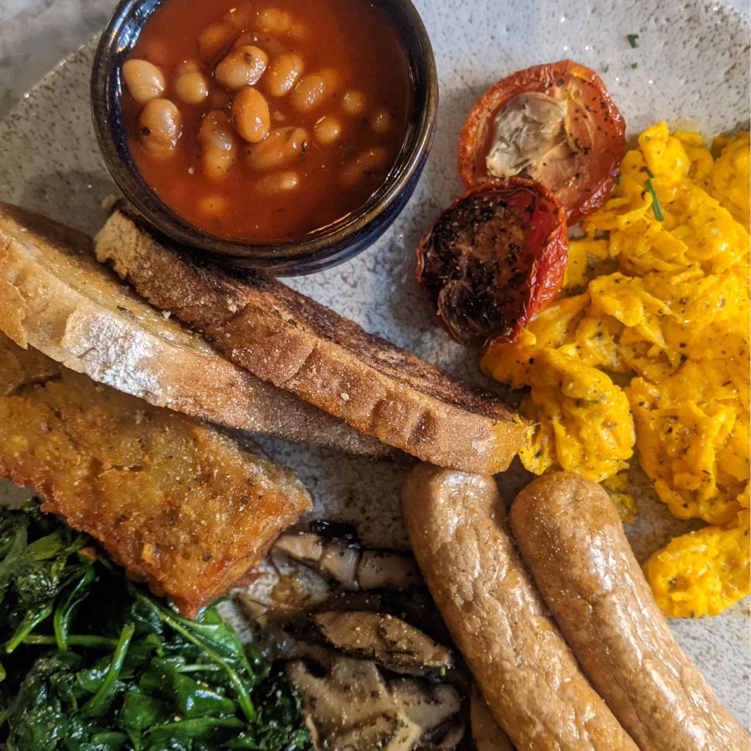 A blue plate filled with eggs, spinach, has browns, beans and vegetarian sausages at Cellar in Hammersmith, one of the best places to get a unique breakfast in london