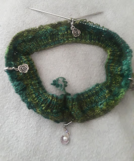 1 by 1 ribbing knit in fingering-weight varegated green yarn; on a circular needle with several stitch markers.