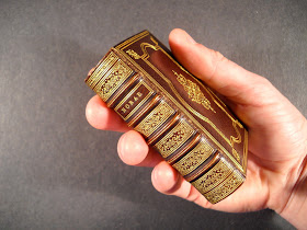 A photograph of a hand holding a small leather book with gold stamping.