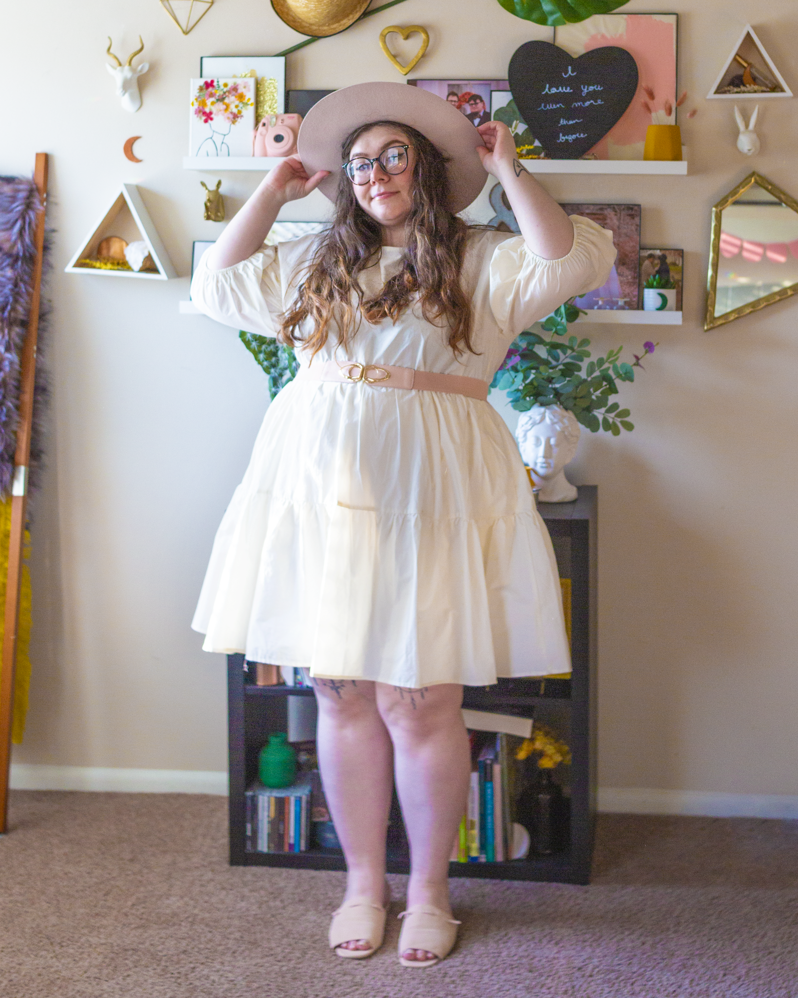 An outfit consisting of a beige wide brim porkpie hat, a white puffy mini dress with 3/4 sleeves, pastel pink belt and pastel pink slide sandals.