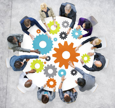 View from above of 12 team members around a table trying to fit different-sized gears together