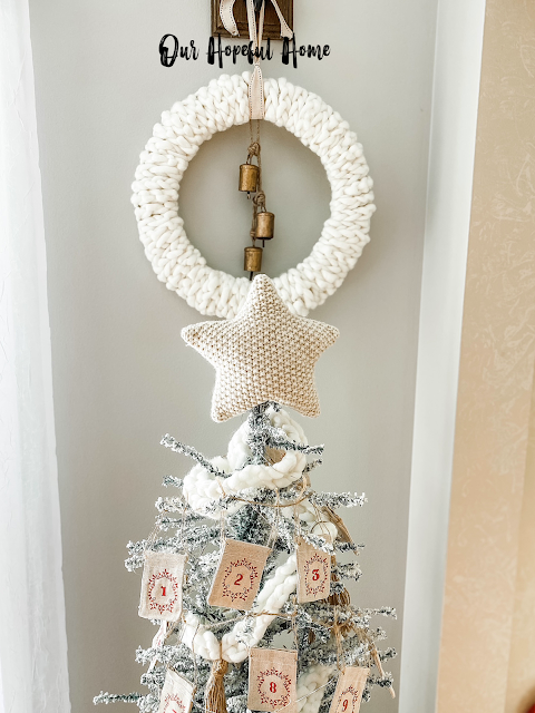 white chunky knit wreath with bells hanging over neutral Christmas tree and star topper