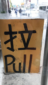A storefront door has a sign affixed to it in Mandarin Chinese and in English for "Pull" 