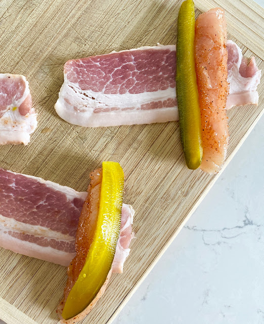 Chicken, bacon and pickles laying on a wooden cutting board to be assembled.