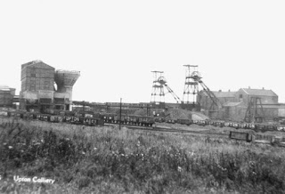 A black and white photo of Upton Colliery, showing long coal trucks, 2 tall mine shafts and some associated buildings