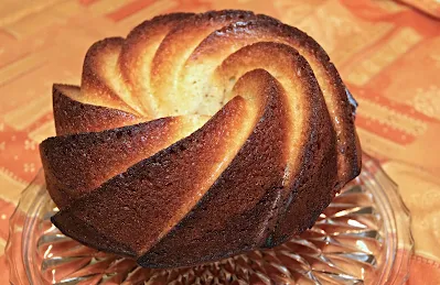 Auf dem Bild ist ein frischgebackener Gugelhupfkuchen auf einem Kuchenteller zu sehen. Der Kuchen wurde leicht mit Puderzucker bestäubt.