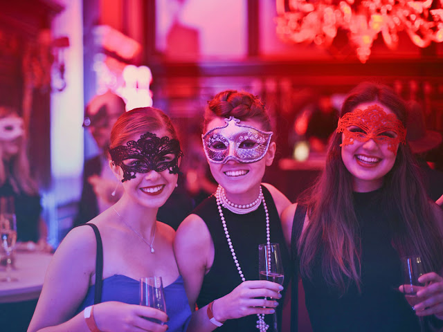 Three women wearing Mardi-gras masks at a party