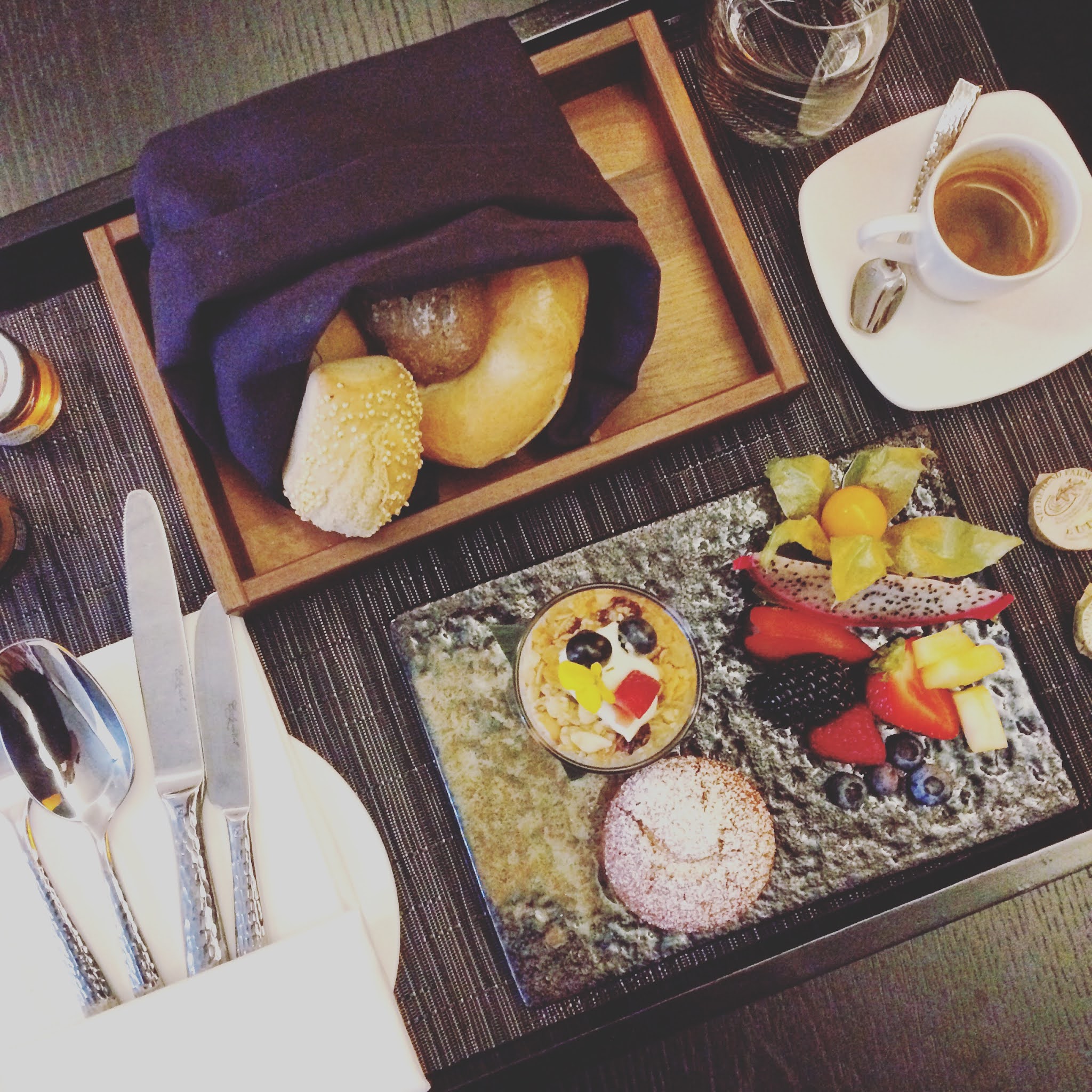 A continental breakfast of bread, pastries and fruits on a wooden tray in a bedroom at the Nobu Shoreditch Hotel, one of the best places for an early london breakfast