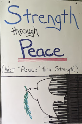 home-made poster. Text: Strength through Peace (Not "Peace" thru Strength). Image of dove holding olive branch