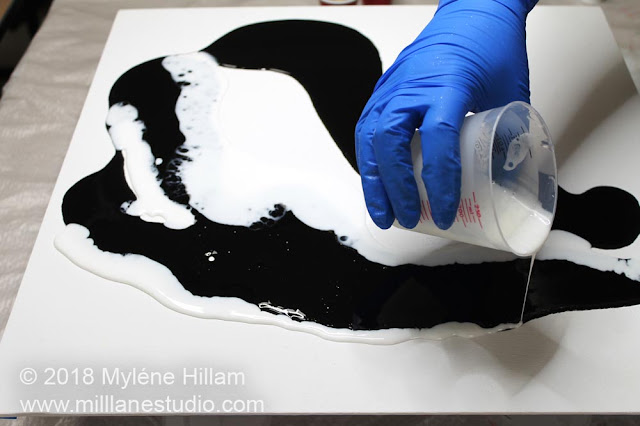 Pouring white resin onto the canvas so that the black and white resin can react.