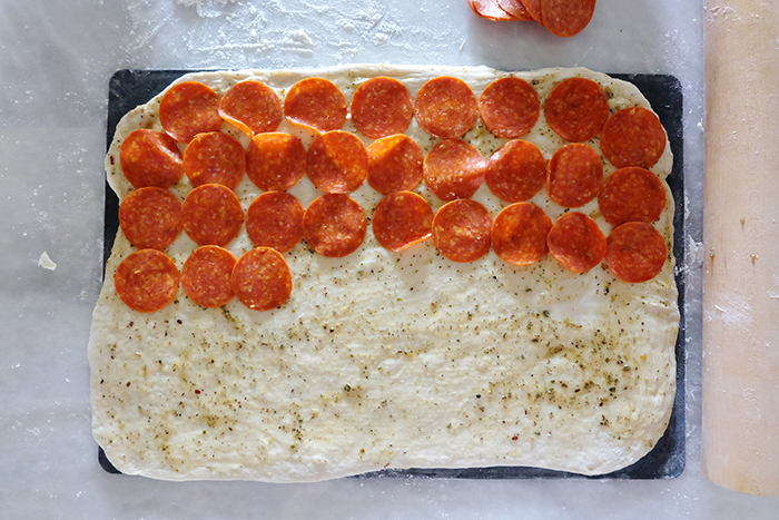 layering pepperoni atop dough