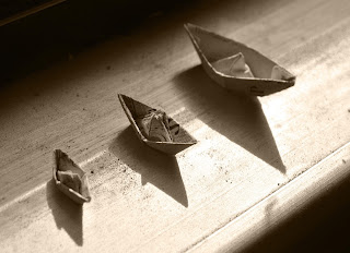 Três barquinhos de papel um do lado do outro, um pequeno, um médio e um grande.