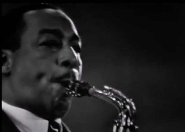 Screenshot of a video of Johnny Hodges playing his saxophone from 1958. It shows a close up of his face and top of the sax.