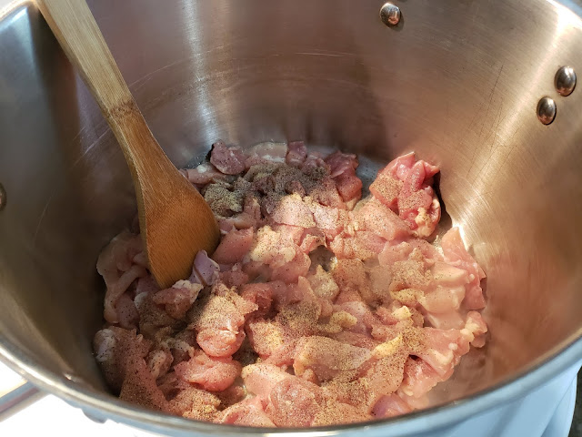 Stainless steel pot and wooden spoon stirring chicken pieces .