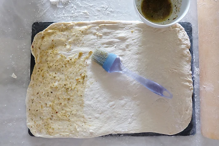 pizza dough rolled out on silicone mat brushed with butter and herbs