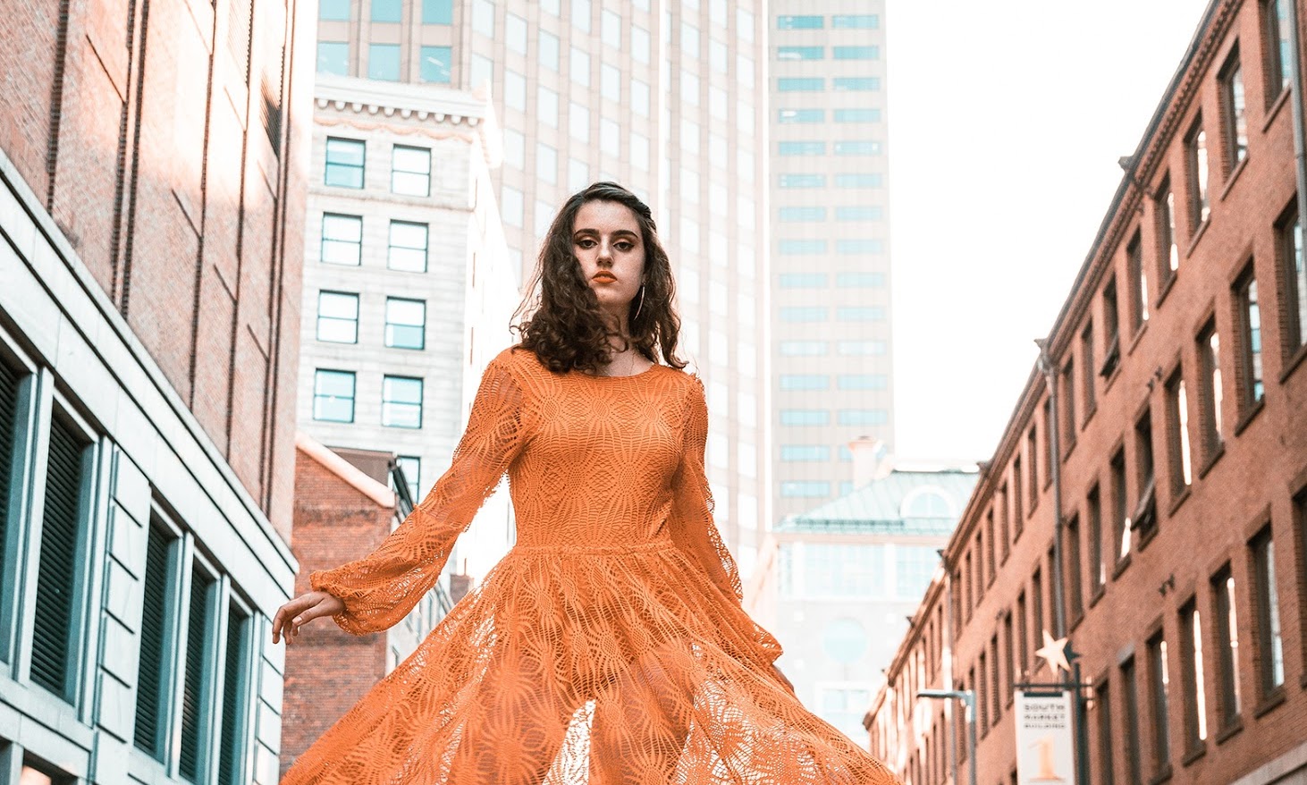 Fashionable woman in an orange dress twirls in a city street