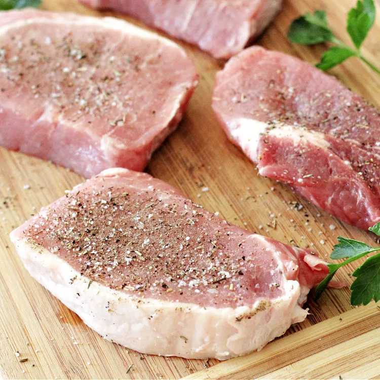 pork chops seasoned and raw on a board ready for the recipe