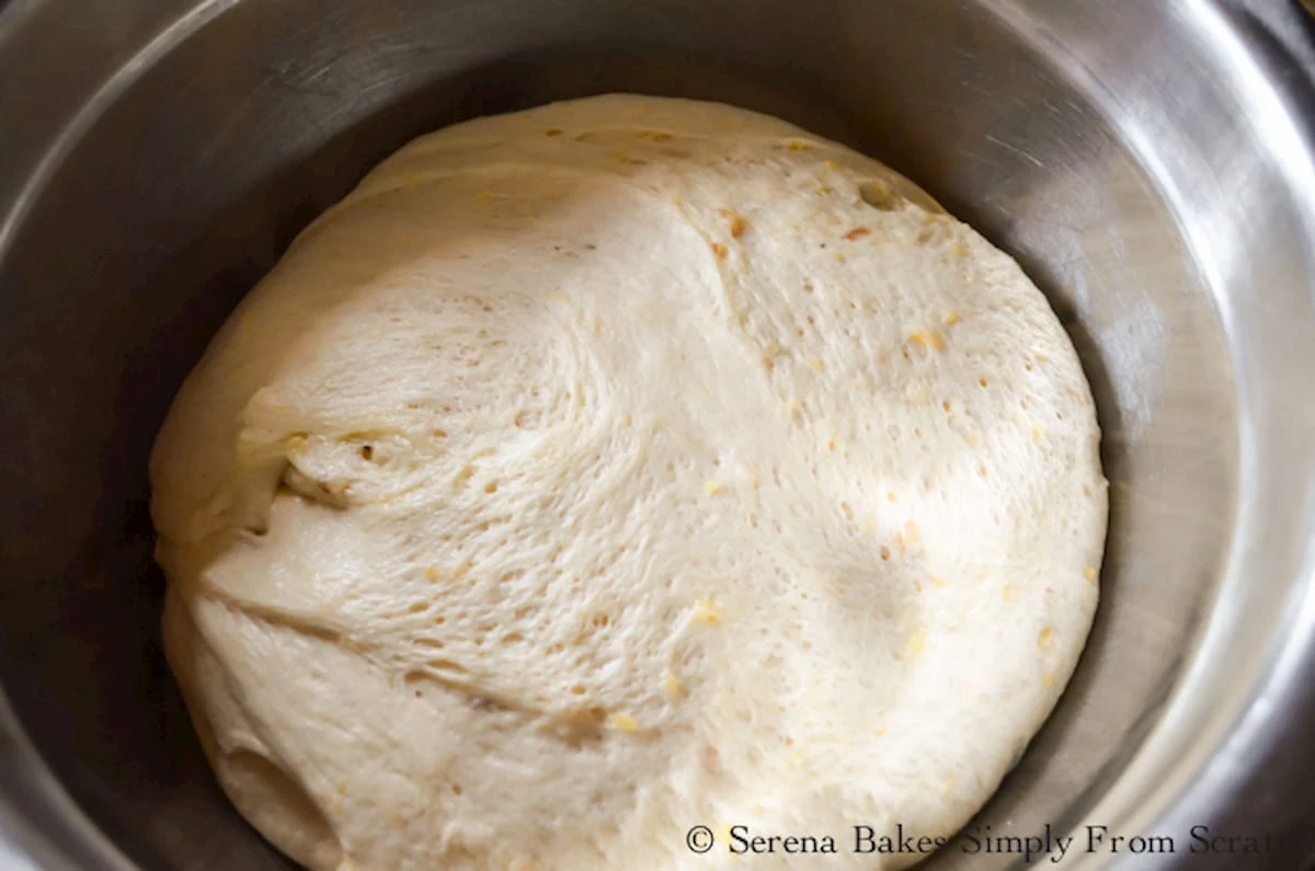 Rised Cheddar Cheese Bun dough in a stainless steel bowl.